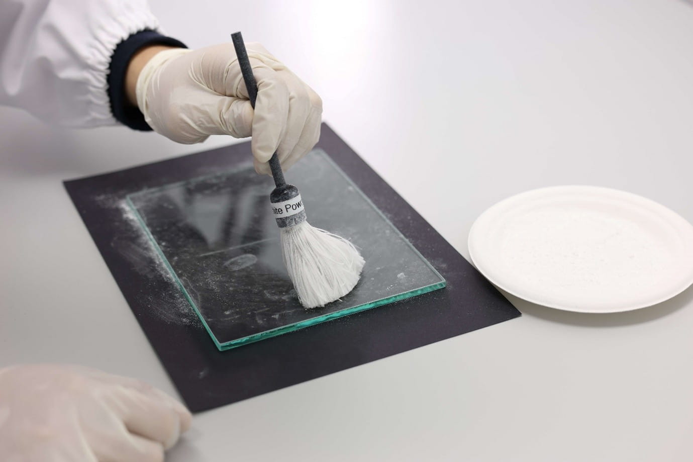 A hand using a brush to dust a glass surface.